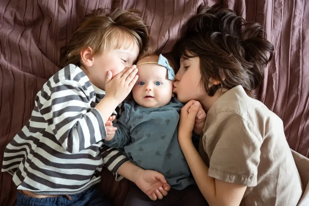 Sibling kissing baby on the cheeks