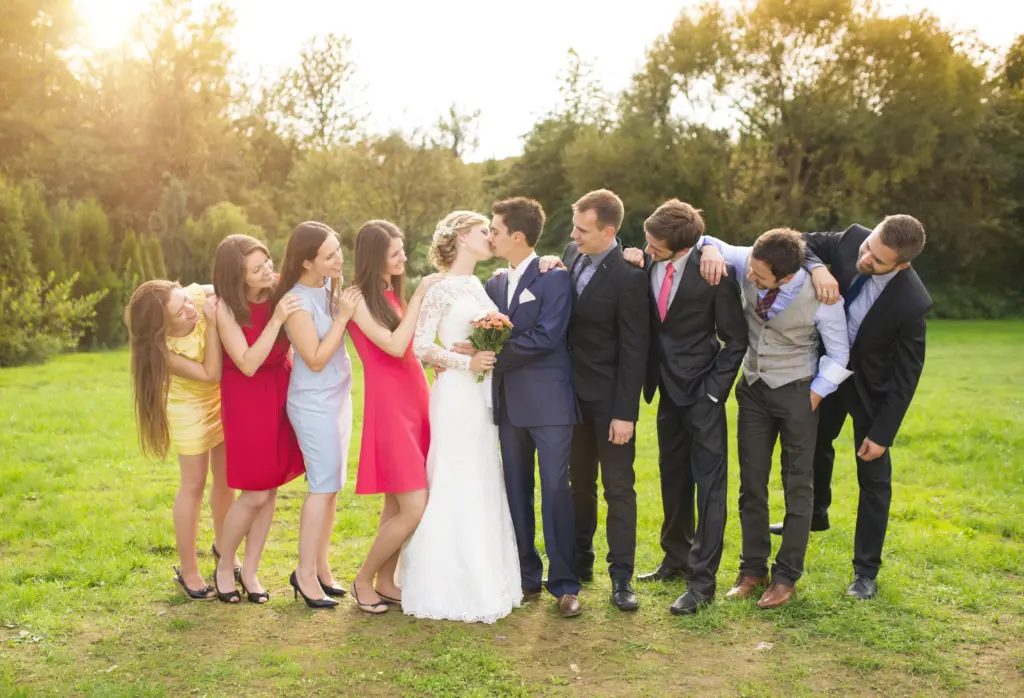 20+ Creative Group Wedding Photo Ideas for Family and Friends 57 Portrait Of Newlywed Couple Kissing Posing With Bridesmaids And Groomsmen