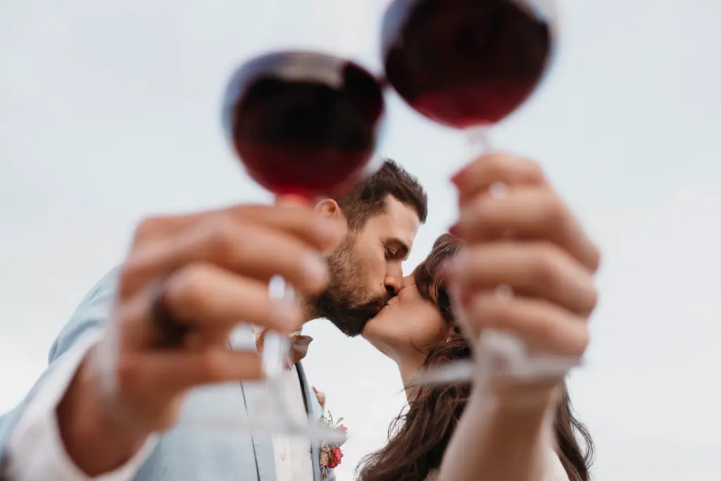 A Sweet Newlywed Kiss Framed by Wine Glasses